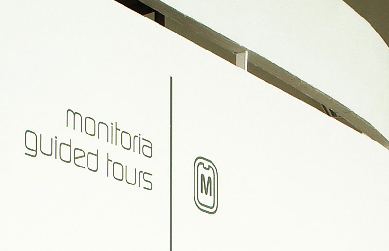 Sinalização bilíngue de monitoria e visitas guiadas da 26ª Bienal de São Paulo, com tipografia, linha divisória e pictograma desenvolvidos para o sistema de orientação do evento.
