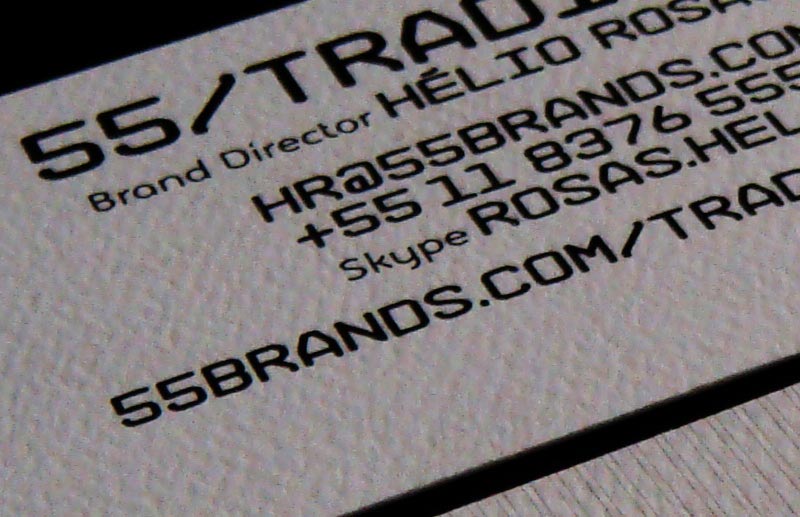 Close-up do cartão institucional 55_Trading, parte do sistema de identidade 55_Brands, com logo, nome de Hélio Rosas, informações de contato e tipografia técnica preta sobre papel texturizado.