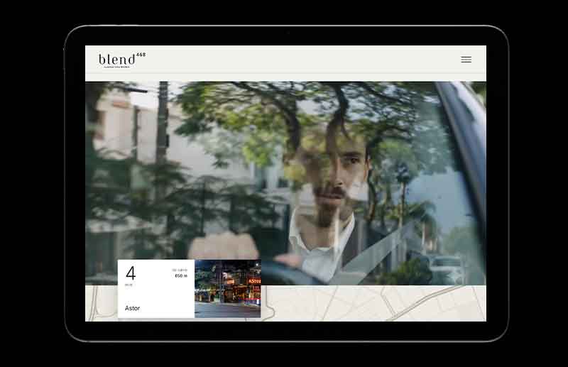 Seção do website Blend 468 com vídeo de um homem dentro de um automóvel, visto através do vidro com reflexos de árvores e da paisagem urbana. Na parte inferior, um módulo apresenta um ponto de interesse do entorno, reforçando a relação do empreendimento com o lifestyle dos Jardins.