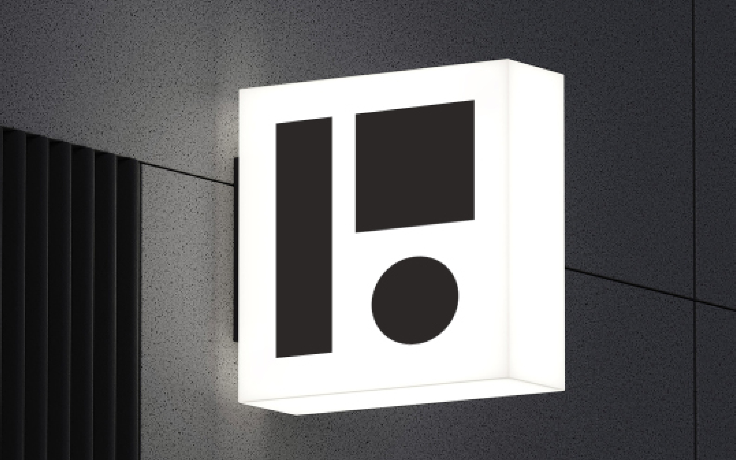 Patio Brasil geometric symbol applied to an illuminated signage panel on a dark wall. The application enlarges the minimalist symbol and demonstrates its use as an identification element in architecture and physical environments.