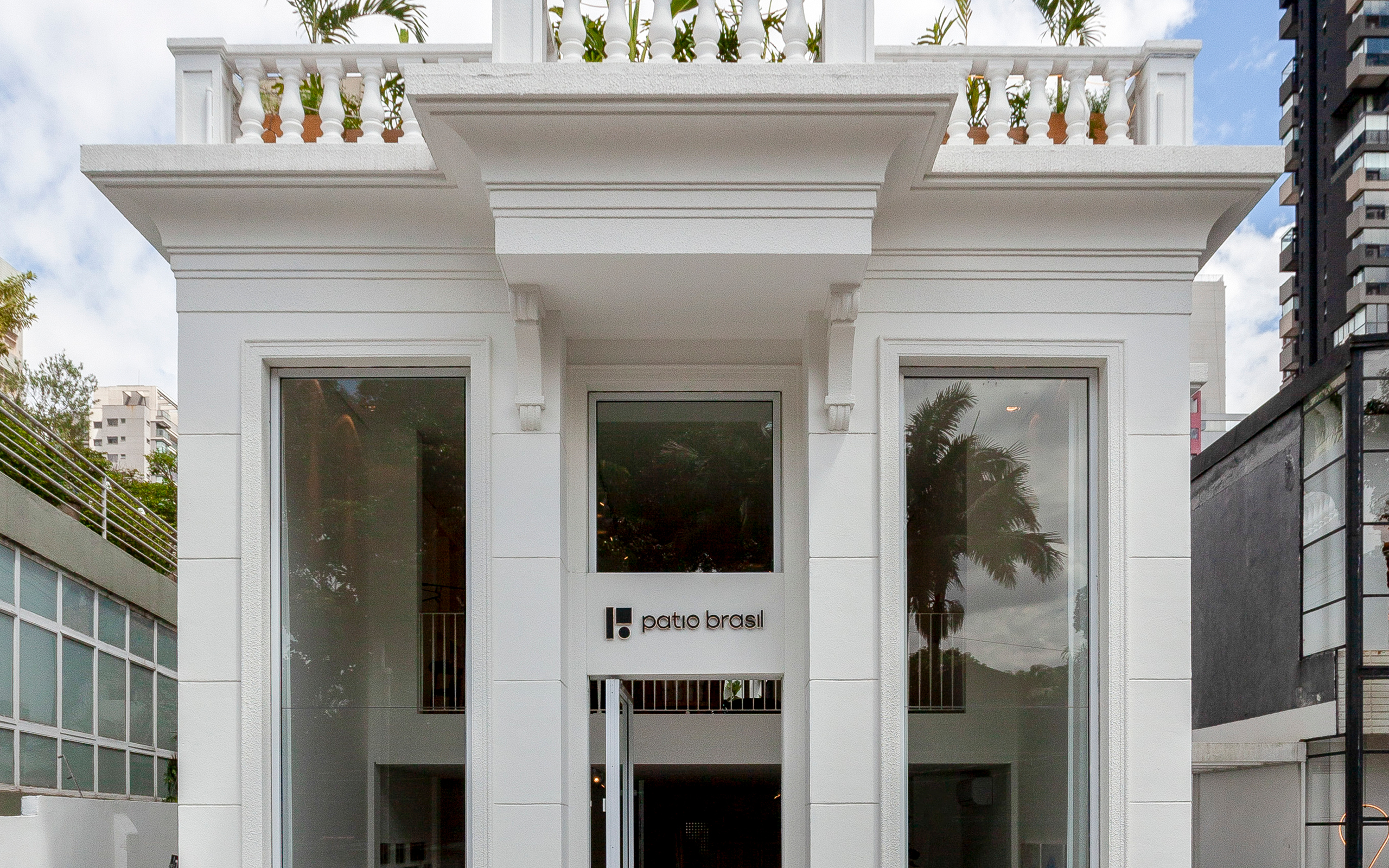 Patio Brasil store façade in a white building with large glass surfaces and the brand identity positioned above the main entrance. Application of the visual identity across commercial architecture, signage and the brand’s physical space.